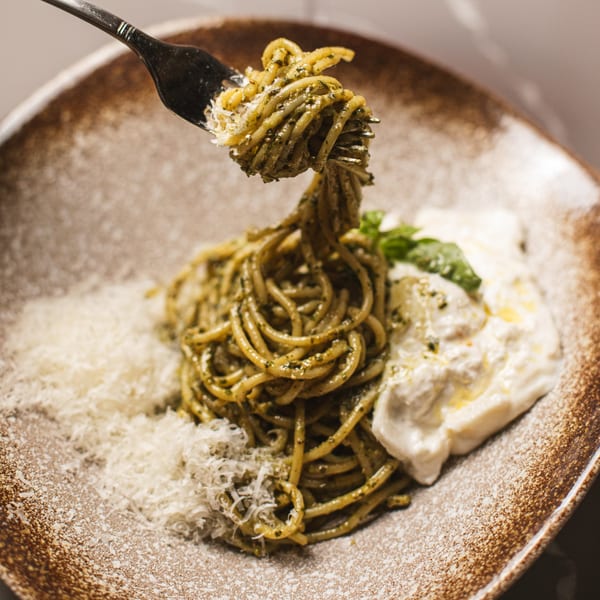 Fork lifting pesto spaghetti from a plate with burrata, basil, and grated cheese.