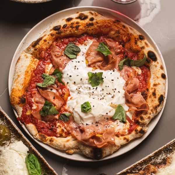 A da Tino. Italian pizza with tomato sauce, prosciutto, burrata, basil, and black pepper.