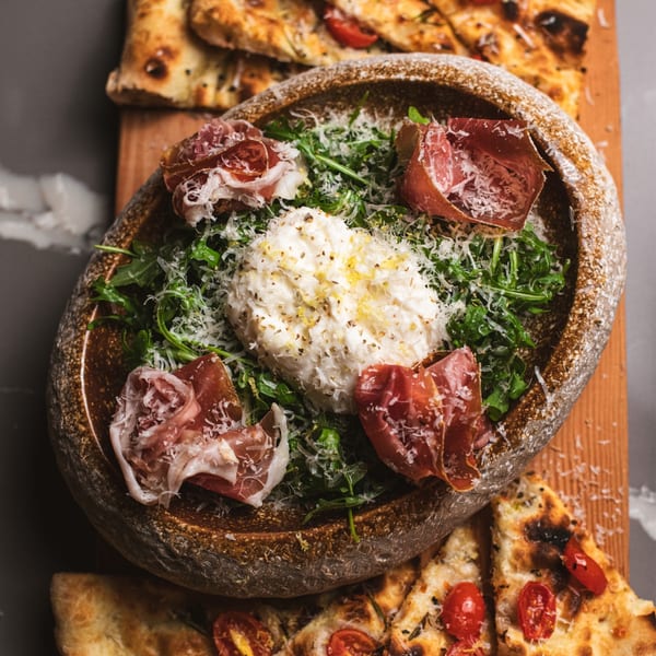 Burrata salad with prosciutto, arugula, and grated cheese in a bread bowl, with focaccia.