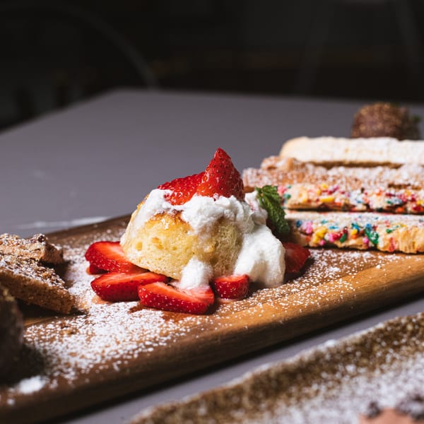 Italian dessert with strawberries, whipped cream, and powdered sugar on a wooden board.
