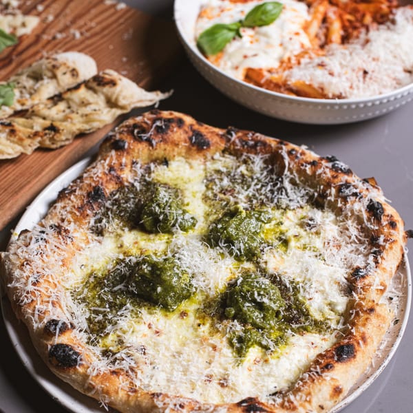 A da Tino. pesto pizza with charred crust and grated cheese, alongside pasta and flatbread.