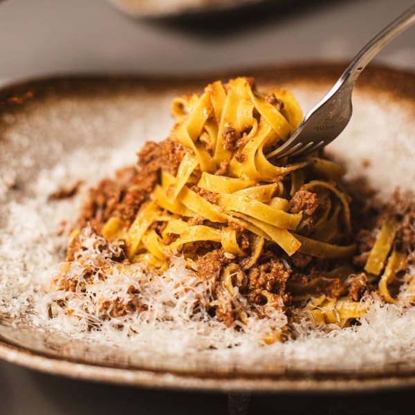 Close-up of da Tino's tagliatelle bolognese with grated parmesan cheese, a fork twirling pasta.